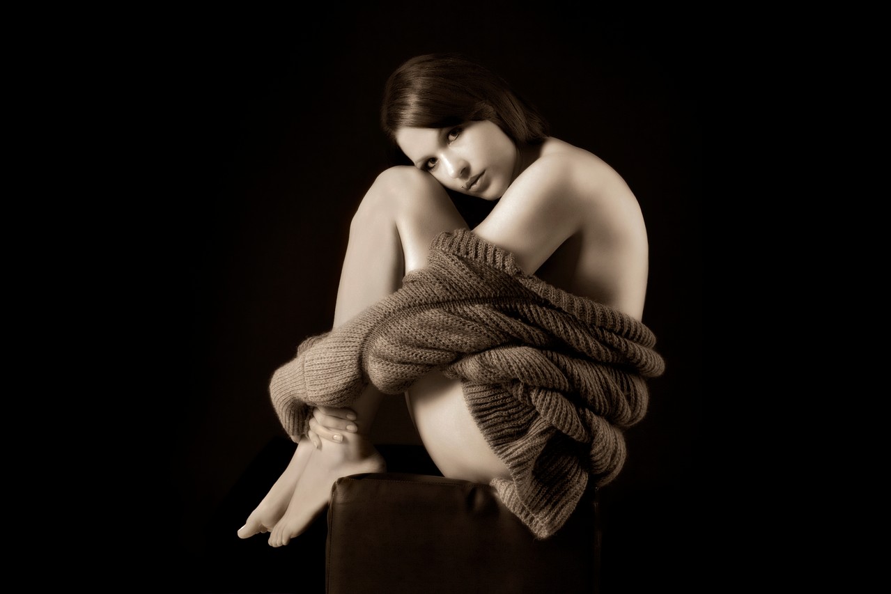 Aktfotografie - Eine junge Frau sitzt auf einem Hocker vor einem schwarzen Hintergrund im Fotostudio