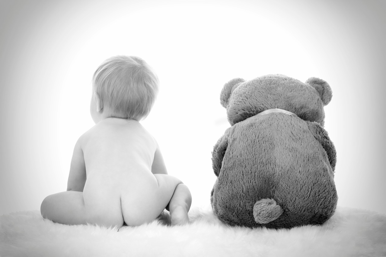 Einen Baby und ein Taddy sitzen auf einem Schaffell