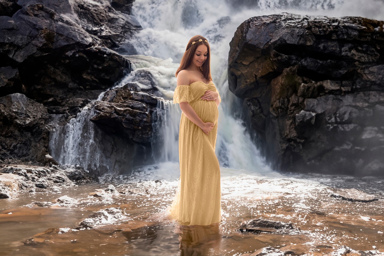 Die werdende Mutter posiert im Babybauchkleid vor einem Wasserfall – Babybauchshooting