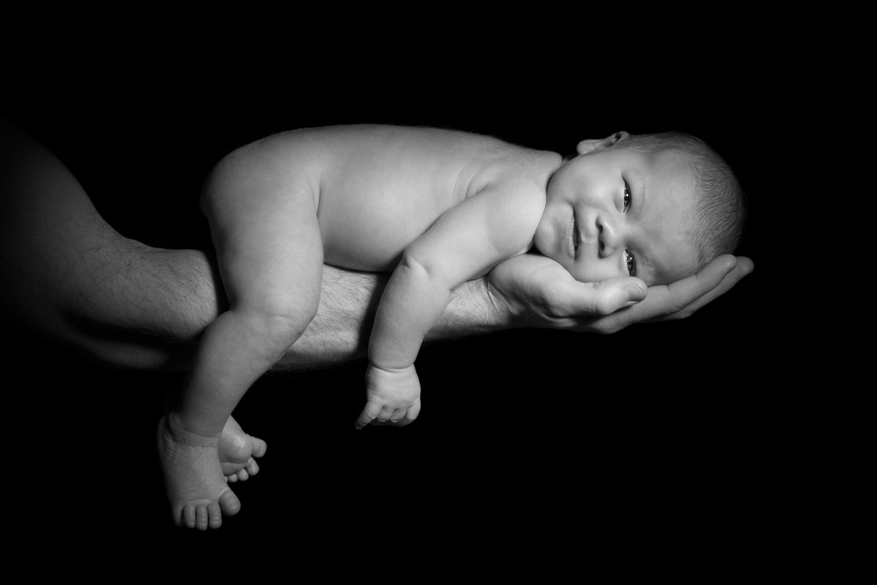 Newbornfotografie - Ein Baby wird vom starken Arm seines Vaters gehalten