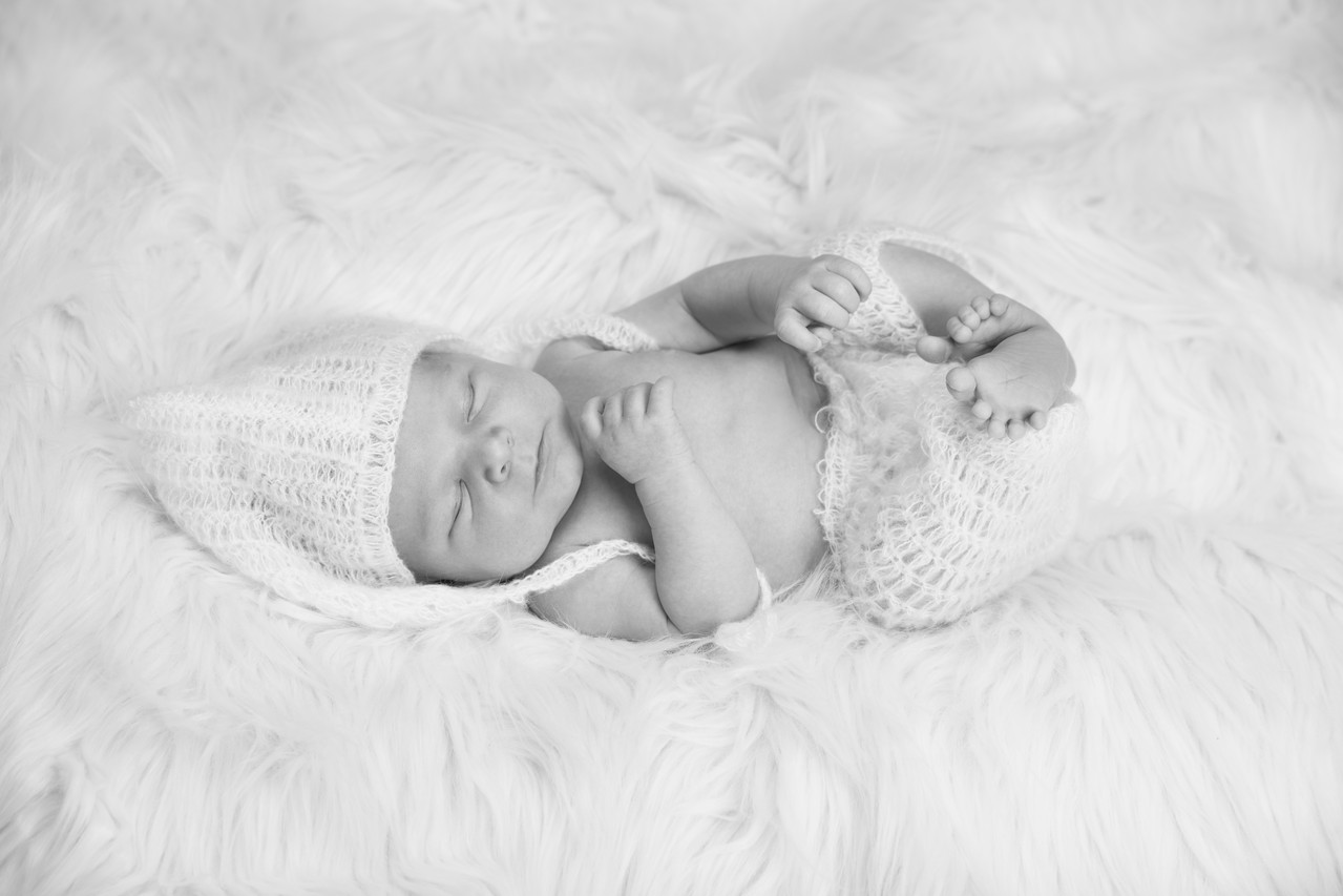 Newbornfotografie - Ein Säugling liegt in zarter Strickkleidung auf einer Felldecke